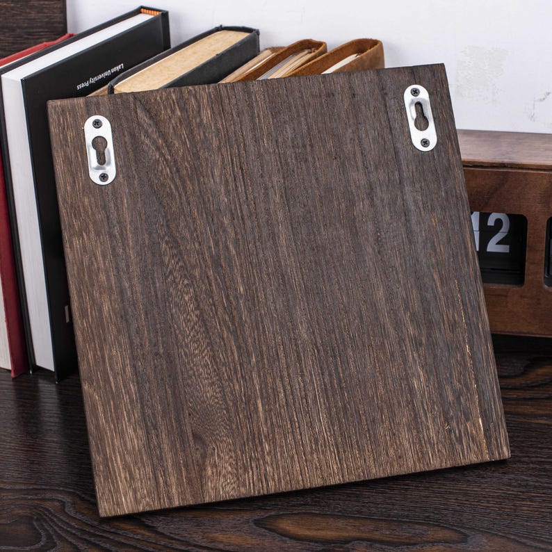 Puede incluir: Una estanter&iacute;a de pared de madera marr&oacute;n oscuro con dos ganchos met&aacute;licos en la parte posterior. La estanter&iacute;a est&aacute; dise&ntilde;ada para ser montada en una pared.