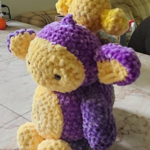 May include: A handmade plush toy in the shape of a monkey. The toy is primarily purple with yellow accents on the face, ears, hands, and feet. The plush is made of a soft, textured material.