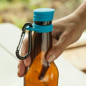 May include: A brown glass bottle with a blue silicone cap and a black carabiner clip attached. The bottle is held by a hand, suggesting portability and convenience. The design is simple and functional.
