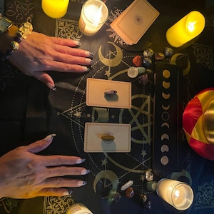 Puede incluir: Un pa&ntilde;o negro con un patr&oacute;n dorado y negro, dos cartas de tarot, un cuenco peque&ntilde;o y cuatro velas encendidas. Tambi&eacute;n hay varios cristales y piedras esparcidos por el pa&ntilde;o.