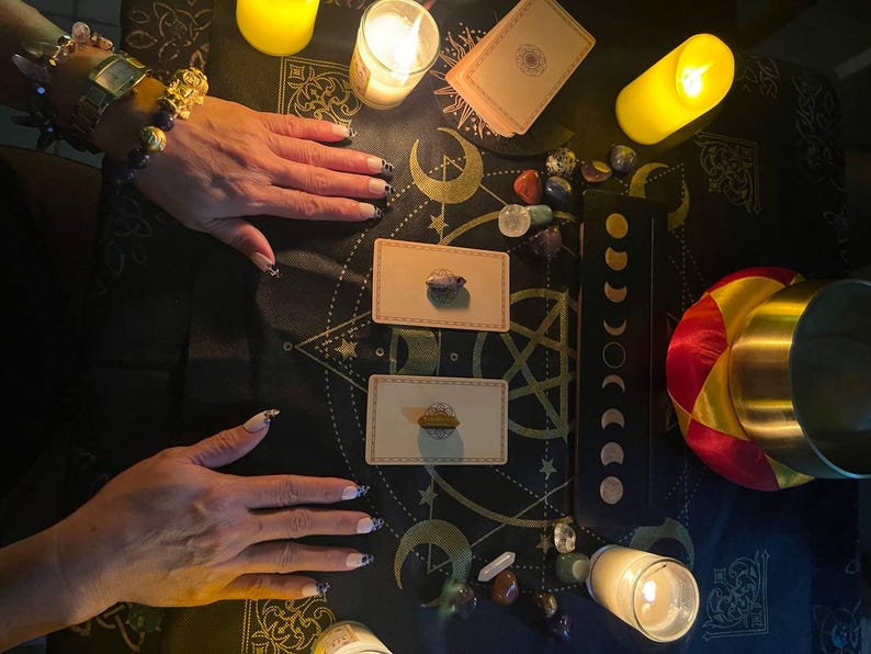 Puede incluir: Un pa&ntilde;o negro con un patr&oacute;n dorado y negro, dos cartas de tarot, un cuenco peque&ntilde;o y cuatro velas encendidas. Tambi&eacute;n hay varios cristales y piedras esparcidos por el pa&ntilde;o.