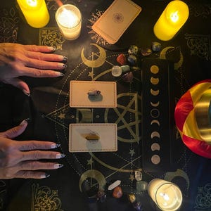 Pu&ograve; includere: Una tovaglia da altare nera con motivi celesti dorati, due carte dei tarocchi sormontate da cristalli, una tavola delle fasi lunari nera, gemme levigate, tre candele a colonna gialle accese e una campana tibetana con bordo dorato.