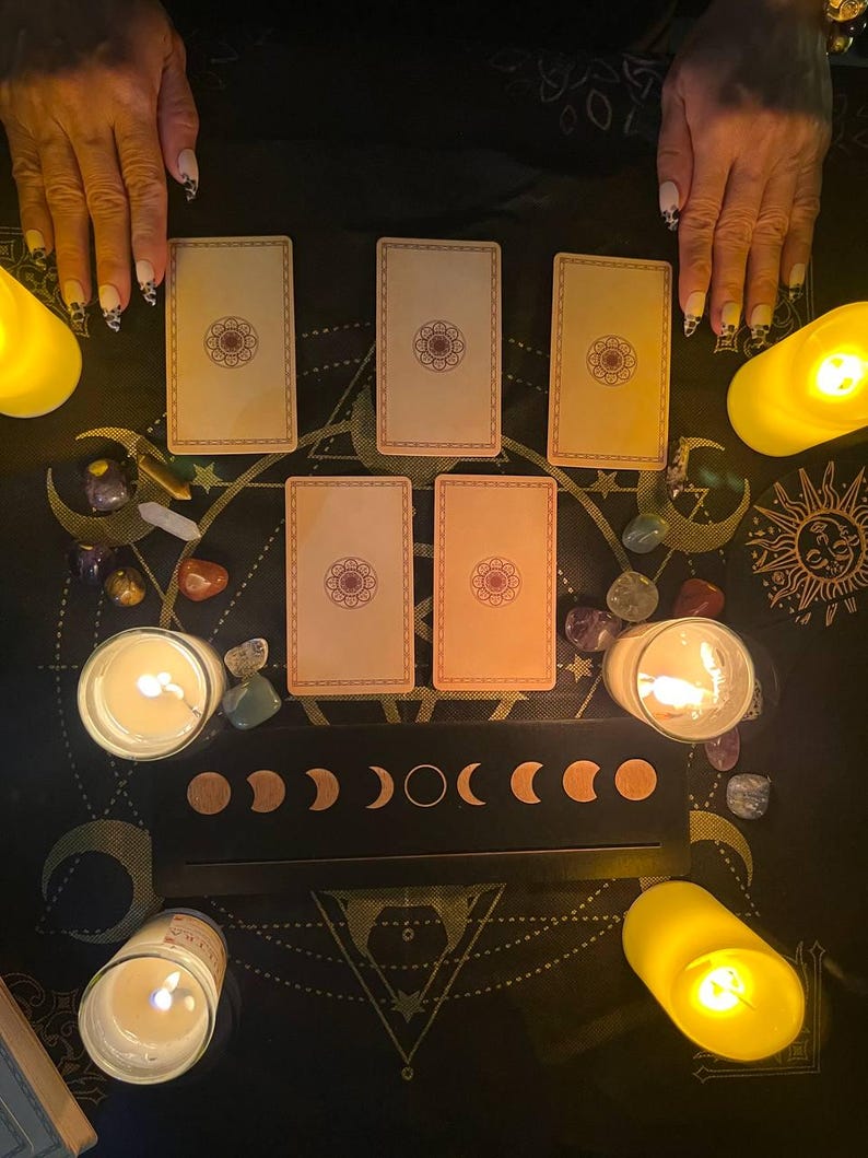 May include: A tarot card reading spread with six cards laid out on a black surface with a moon phase design. There are candles and crystals surrounding the cards.