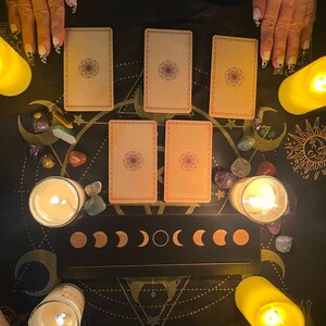 Peut inclure: Un &eacute;talement de cartes de tarot avec cinq cartes dispos&eacute;es sur une surface noire avec un tableau des phases lunaires et des bougies. Les cartes sont de couleur cr&egrave;me avec un motif brun au centre.