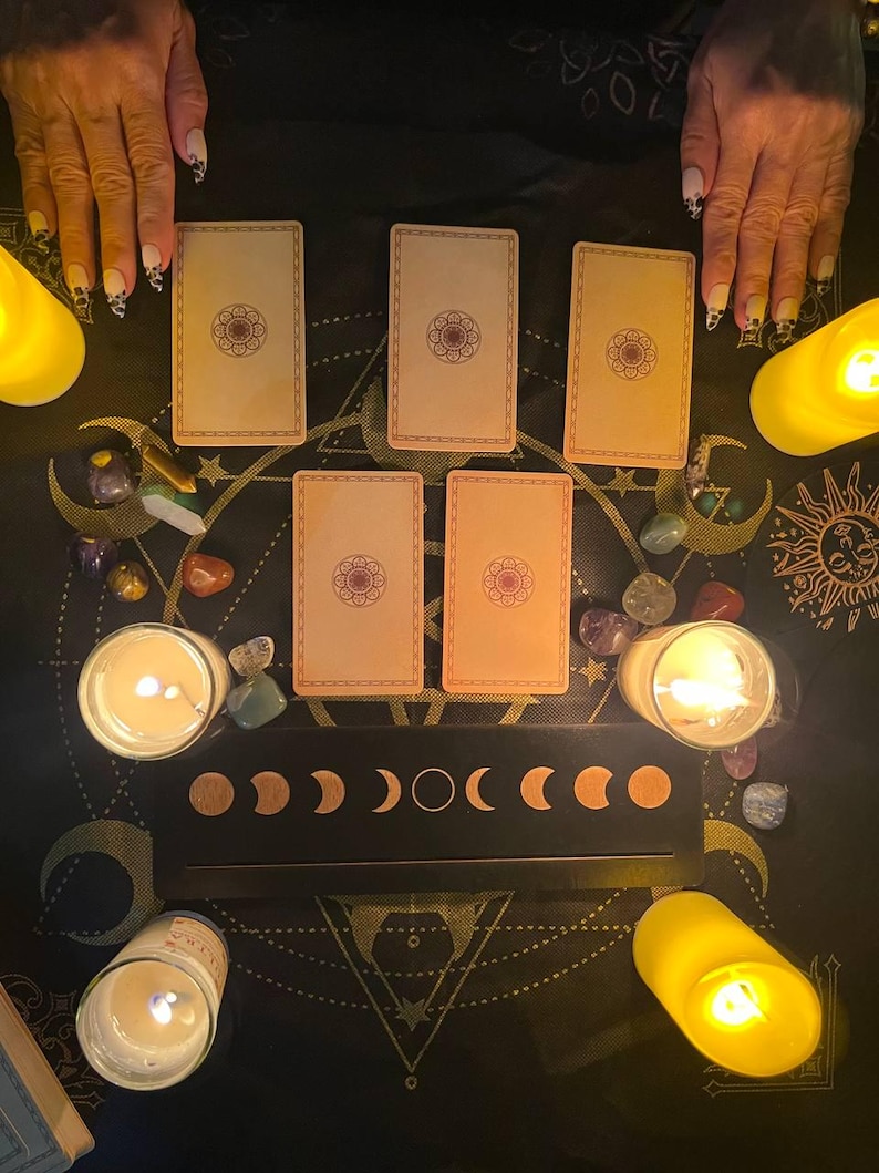 Peut inclure: Un &eacute;talement de cartes de tarot avec cinq cartes dispos&eacute;es sur une surface noire avec un tableau des phases lunaires et des bougies. Les cartes sont de couleur cr&egrave;me avec un motif brun au centre.