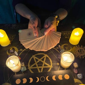 Peut inclure: Une nappe de table noire avec un pentagramme dor&eacute; et un motif de phases lunaires. Il y a des bougies, des cristaux et un jeu de cartes de tarot &eacute;tal&eacute;s sur la table.