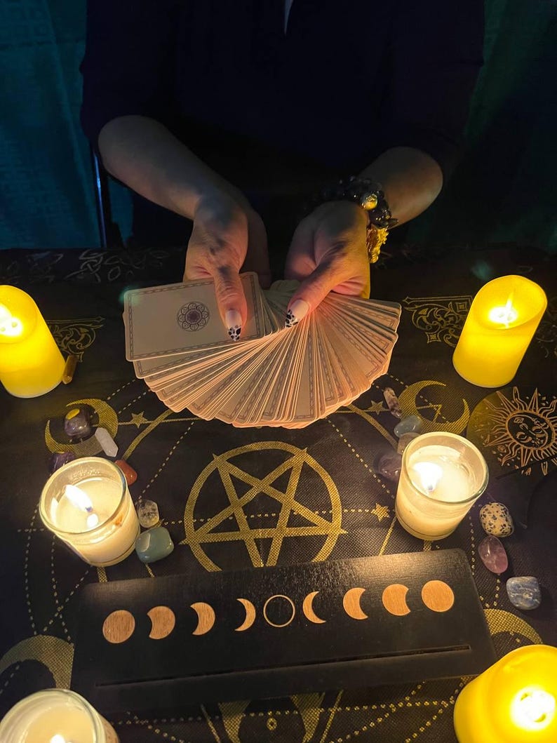 Peut inclure: Une nappe de table noire avec un pentagramme dor&eacute; et un motif de phases lunaires. Il y a des bougies, des cristaux et un jeu de cartes de tarot &eacute;tal&eacute;s sur la table.