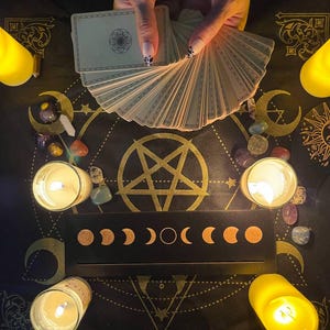 May include: A black cloth with a pentagram design, surrounded by candles and crystals. A deck of tarot cards is fanned out in the center of the cloth.