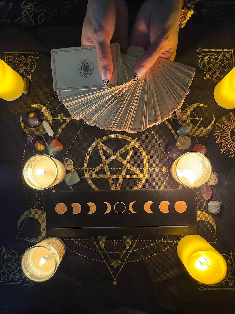 May include: A black cloth with a pentagram design, surrounded by candles and crystals. A deck of tarot cards is fanned out in the center of the cloth.