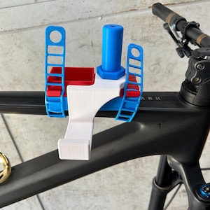May include: A multi-colored bicycle accessory, mounted on the handlebars. The accessory is primarily white, blue, and red, with a cylindrical blue component and a rectangular red section. The bicycle frame is black, with a gold-colored accent.