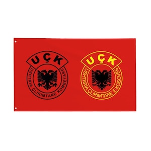 May include: A red flag featuring two circular emblems with a black double-headed eagle and text. The emblems are in black and yellow, with the text "UÇK" at the top and other text around the eagle.