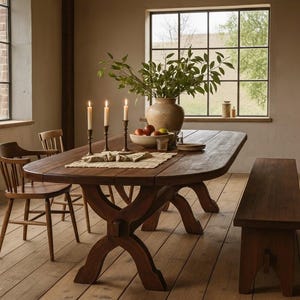 Puede incluir: Un comedor rústico con una gran mesa ovalada de madera oscura, dos sillas de madera y un banco. La mesa está decorada con velas, un jarrón con vegetación y un cuenco de fruta. La habitación tiene grandes ventanas.