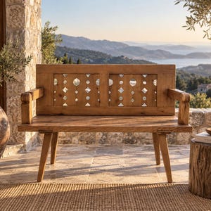 May include: A wooden bench featuring a backrest with two rectangular panels containing cut-out geometric shapes, including circles and diamonds. The bench has four angled legs, two armrests, and a natural brown wood grain finish throughout.