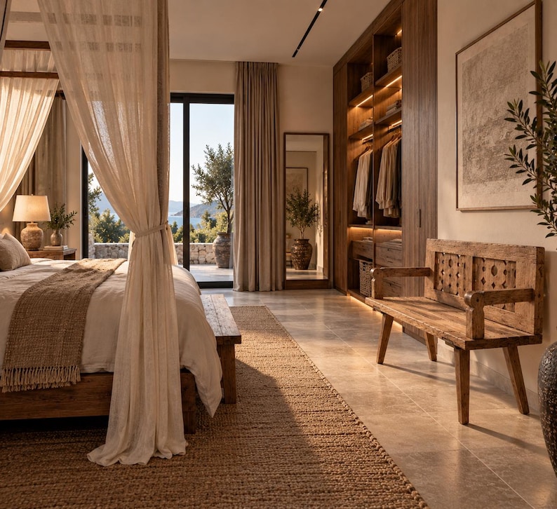 May include: A bedroom interior featuring a four-poster bed with light beige curtains, a wooden bench with a carved backrest, a large walk-in closet with integrated lighting, a full-length mirror, and a textured jute rug on a stone floor.
