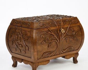 May include: A wooden chest with a carved tree design. The chest is brown, with a curved shape and four short legs. The lid and sides feature detailed carvings of leaves and branches, and a small brass lock.
