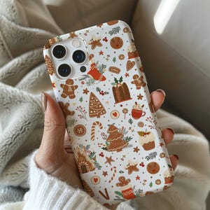 May include: A white phone case featuring a festive Christmas pattern. The design includes gingerbread men, Christmas trees, candy canes, and other holiday-themed illustrations in brown, red, and green. The case is designed to fit a smartphone.