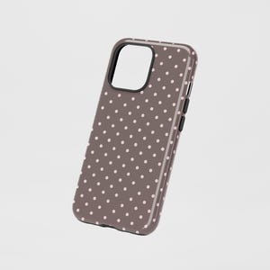 May include: A brown phone case with a pattern of small, evenly spaced, light pink polka dots. The case has a black border around the camera cutout and black buttons on the side. The case is designed to fit a smartphone.