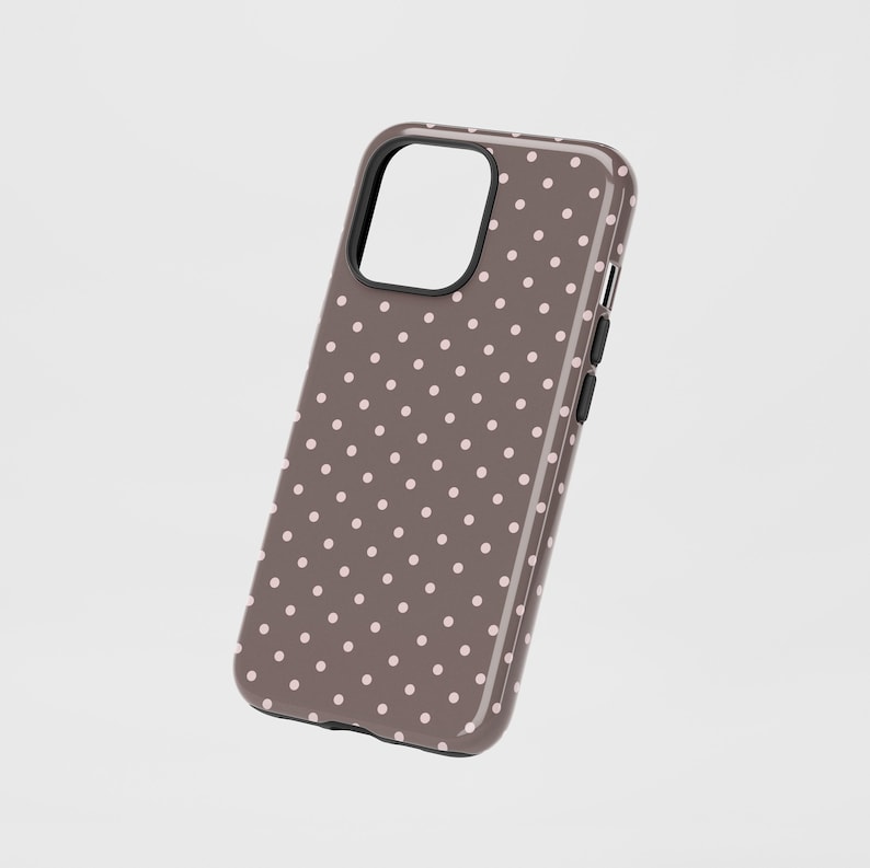 May include: A brown phone case with a pattern of small, evenly spaced, light pink polka dots. The case has a black border around the camera cutout and black buttons on the side. The case is designed to fit a smartphone.
