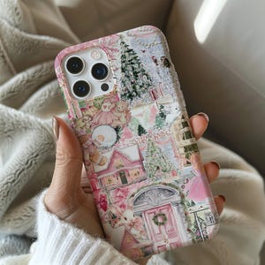Könnte beinhalten: Eine rosa-weiße Handyhülle mit einem Weihnachtsdorf-Design. Die Hülle zeigt rosa Häuser, Weihnachtsbäume und Teddybären. Die Hülle wird in einer Hand gehalten.