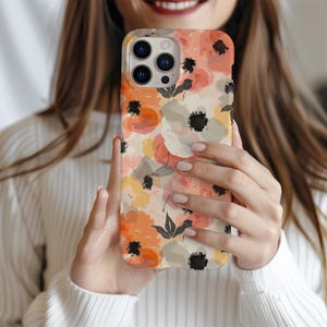 May include: A phone case with a floral pattern. The case features a watercolor-style design with pink, orange, and yellow flowers on a white background. The case has a cutout for the phone's camera.