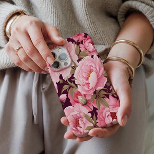 May include: A pink and green floral phone case with a dark background. The case features a variety of pink peonies and green leaves.