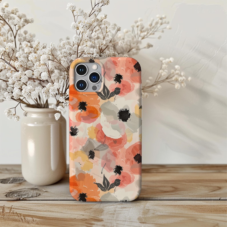 May include: A phone case with a floral pattern featuring pink, orange, and yellow flowers on a white background. The case has a cutout for the camera lens.