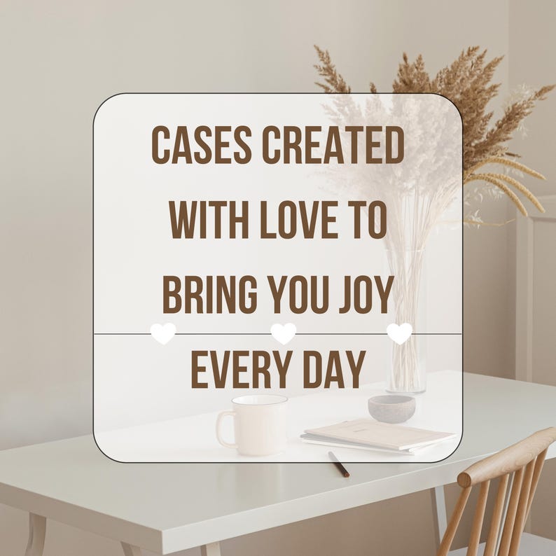 May include: A white rectangular sign with rounded corners displays the text "CASES CREATED WITH LOVE TO BRING YOU JOY EVERY DAY" in brown. Three white hearts are below the text. A mug, bowl, and book are on the table.