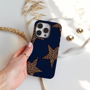 May include: Navy blue phone case with a leopard print star design. The case has a dark blue background with two large stars in a brown and black leopard print pattern. The phone case is held by a hand.