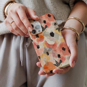 May include: A phone case with a floral pattern in shades of orange, pink, and yellow. The case has a watercolor effect and features black accents.