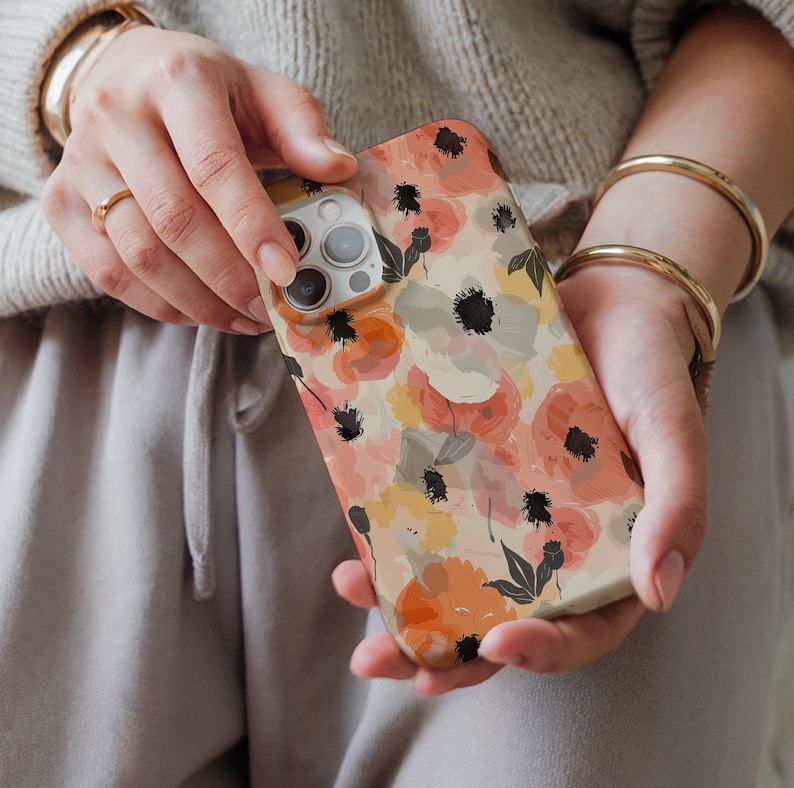 May include: A phone case with a floral pattern in shades of orange, pink, and yellow. The case has a watercolor effect and features black accents.