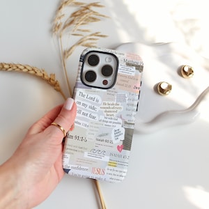 May include: A phone case with a collage design featuring Bible verses and inspirational quotes. The case has a black border and a white and gray background with text snippets. The case is held by a hand with a gold ring.