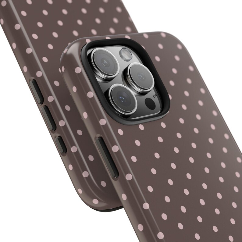 May include: Close-up of two phone cases. The cases are brown with a pattern of small, evenly spaced pink polka dots. The phone case on top has a black border around the camera lenses.