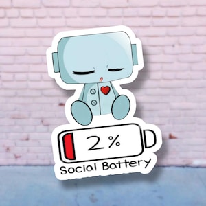 May include: A sticker of a light blue robot with a red heart and closed eyes, above a battery icon showing 2% and the words "Social Battery". The sticker has a white border and is against a brick wall.