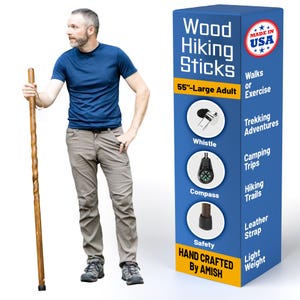 May include: A man stands next to a wooden hiking stick, 55 inches long, with a blue box. The box reads "Wood Hiking Sticks" and "Hand Crafted By Amish." Features include a whistle, compass, and leather strap.