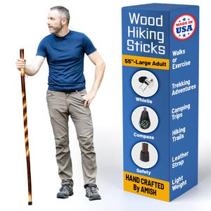 May include: A 55-inch wood hiking stick with a spiral design, held by a person. The stick is dark brown with lighter brown accents. A blue box displays "Wood Hiking Sticks" and features a whistle, compass, and leather strap. Hand crafted by Amish.