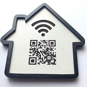 May include: A house-shaped sign with a black border and a white centre. The sign features a black engraved Wi-Fi symbol at the top and a black engraved QR code in the centre. The design is flat and has a distinct outline of a house with a chimney.
