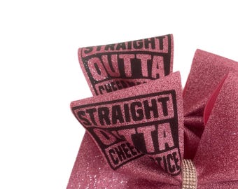 May include: Pink glitter cheer bow with a black and white "Straight Outta Cheer" design and a rhinestone accent.