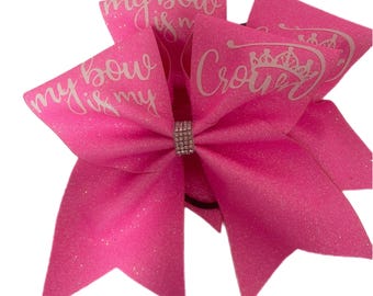May include: Pink cheer bow with white glitter and the text "my bow is my crown" with a rhinestone in the center.