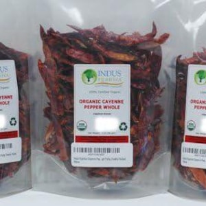 May include: Three clear plastic bags filled with dried, red cayenne peppers. Each bag has a white label with the text "ORGANIC CAYENNE PEPPER WHOLE" and the "INDUS Organics" logo. The packaging is labeled as a "3 pack".