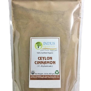 May include: A resealable bag of 16 ounces (453 grams) of Indus Organics Ceylon Cinnamon (C. Zeylanicum). The bag is white with a label that says "Indus Organics" and "Good Health. Organically. 100% Certified Organic". The label also says "Ceylon Cinnamon (C. Zeylanicum)" and "Net Weight: 16 Oz (453 gm)". The bag is on a white background.