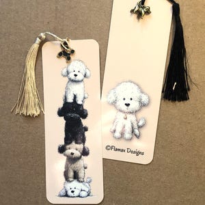 Può includere: Due segnalibri rettangolari con illustrazioni di cani bianchi e neri soffici. Un segnalibro presenta una pila di cani, l'altro ha un singolo cane. Entrambi hanno un ciondolo a forma di cane e un nappa. Il testo "©Flamax Designs" è visibile.