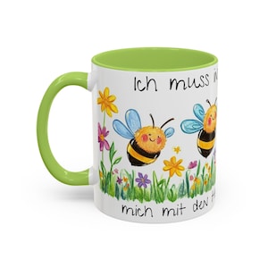 Könnte beinhalten: Weiße Keramiktasse mit grünem Rand. Die Tasse zeigt eine bunte Illustration von Bienen und Blumen mit dem Text "Ich muss mich mit den Bienen beeilen".