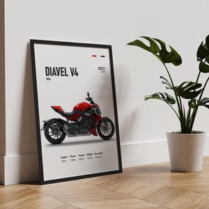 Pu&ograve; includere: Un poster incorniciato in nero con sfondo bianco che presenta una moto Ducati Diavel V4 rossa. Il poster include il testo "Diavel V4" e "Ducati" insieme al motore, la potenza, la coppia, il peso e la velocit&agrave; massima della moto.