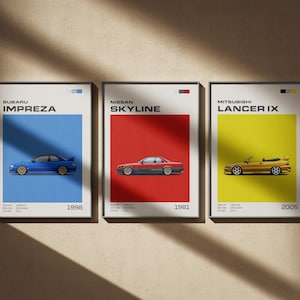 May include: Three framed car posters. The first features a blue Subaru Impreza on a blue background, the second a red Nissan Skyline on a red background, and the third a gold Mitsubishi Lancer IX on a yellow background. Each poster includes the car's name and year.