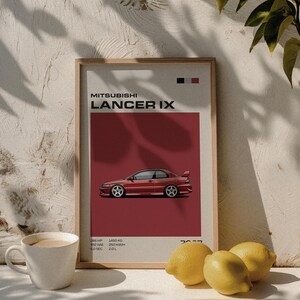 May include: A framed print featuring a red Mitsubishi Lancer IX car illustration. The poster has a red background with the car's profile and technical specifications. A white coffee mug and lemons are in the foreground.