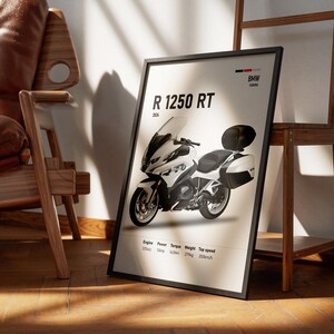 May include: A framed poster featuring a white and black BMW R 1250 RT motorcycle. The poster includes specifications such as engine size, power, torque, weight, and top speed. The poster is leaning against a wall near a wooden chair and a wooden shelf.