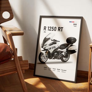 May include: Framed poster featuring a white BMW R 1250 RT motorcycle. The poster includes the model name, year, and specifications like engine size, power, torque, weight, and top speed of 200 km/h. The poster is in a black frame.