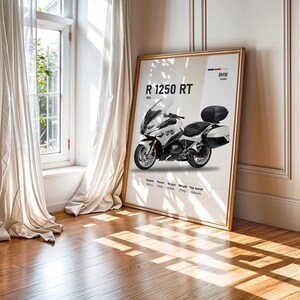 May include: A framed poster featuring a white and black BMW R 1250 RT motorcycle. The poster includes technical specifications and the BMW logo. The poster is displayed on a wooden floor, next to a window with white curtains.