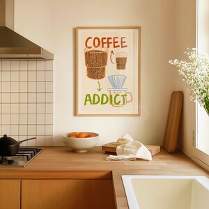 Pu&ograve; includere: Una stampa incorniciata con sfondo bianco e un'illustrazione colorata di una macchina per il caff&egrave; e una tazza di caff&egrave;. Il testo "COFFEE ADDICT" &egrave; scritto in lettere verdi sotto l'illustrazione.
