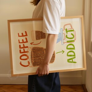 Pu&ograve; includere: Un poster incorniciato con un'illustrazione colorata di una caffettiera e tazze da caff&egrave;. Il testo sul poster recita "Coffee Addict".